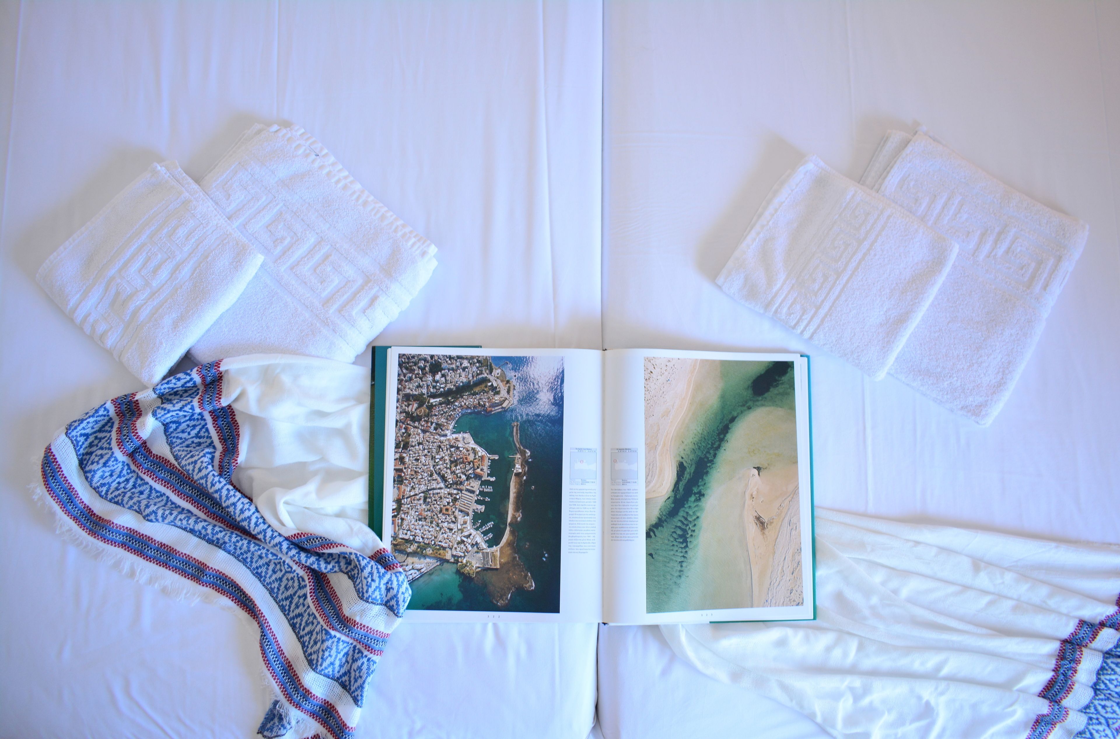A neatly made bed with white linens, a patterned blanket, and a book with a beach scene.