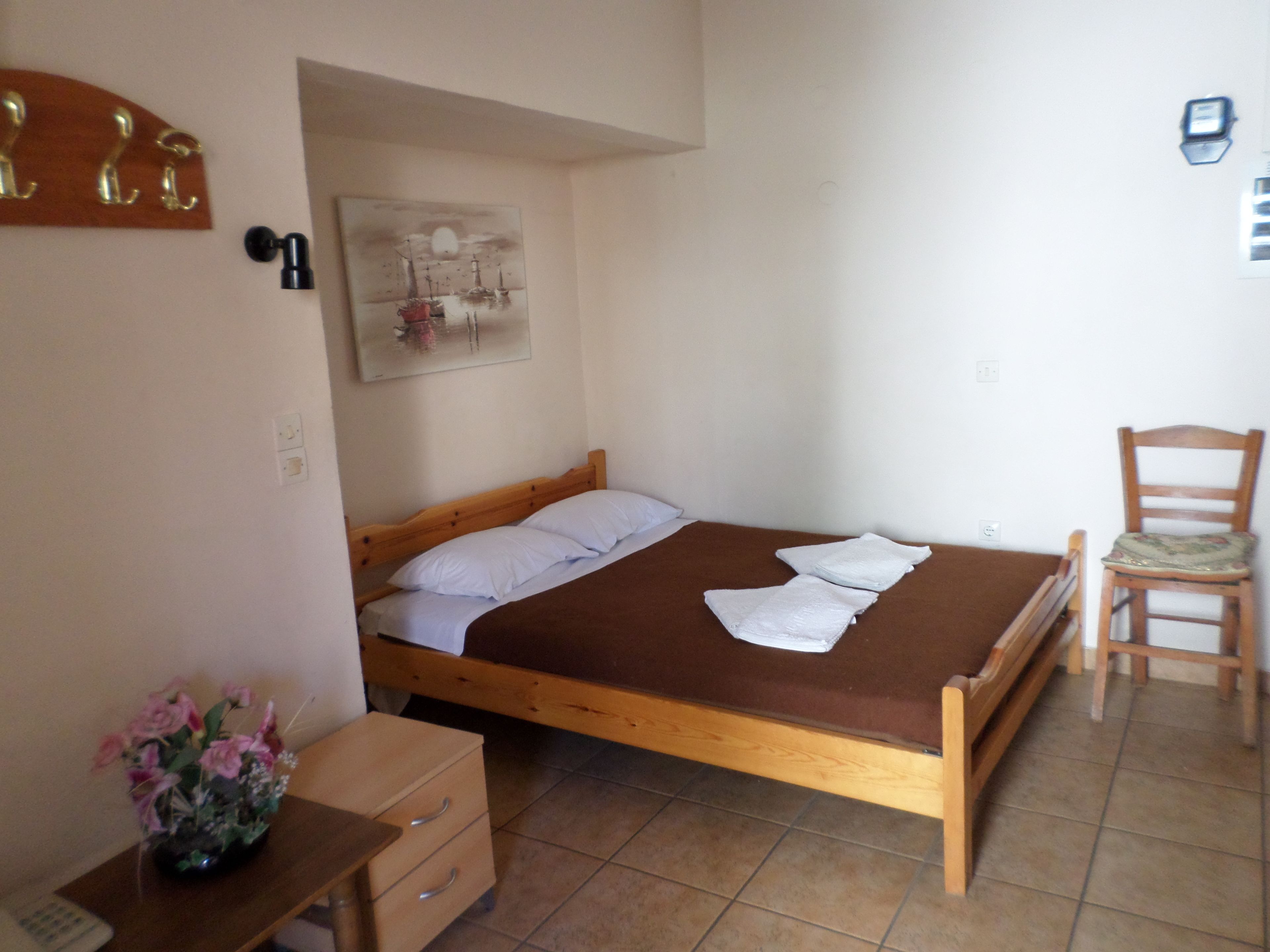 A bedroom with a wooden bed, a small wooden desk, a chair, and a wall-mounted painting.