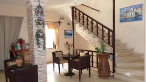 A dining area with a table and chairs, a staircase with a railing, and a wall with a painting. - Tina Economy Hotel (Chania)
