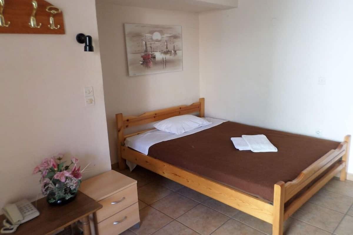 Una cama individual con estructura de madera, una mesita de noche con lámpara, un escritorio pequeño con teléfono y una obra de arte colgada en la pared.