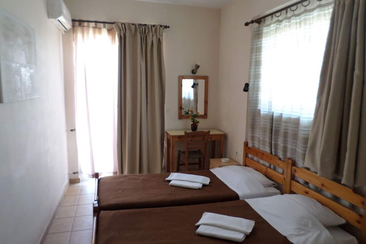 Habitación de hotel con dos camas, un escritorio, una silla, un espejo y una ventana con cortinas.