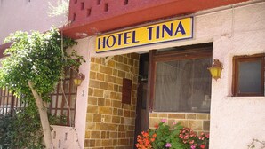 A building with a sign reading "HOTEL TINA" above the entrance. There are steps leading up to the door, and potted plants with flowers are placed outside. - Tina Economy Hotel (Chania)