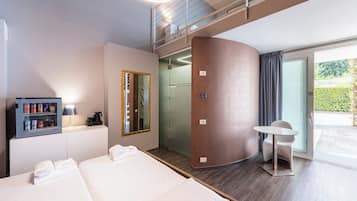 A modern hotel room with a bed, a minibar, a mirror, a bathroom, and a balcony.