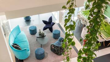 Een moderne lounge met diverse zithoeken, waaronder een grote blauwe bank, ronde poefs en een bijzondere fauteuil met een bloemenprint.