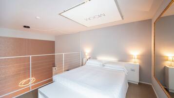 A modern hotel room with a large bed, bedside lamps, a mirror, and a ceiling light fixture.
