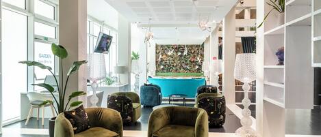A modern lobby with green armchairs, a round table, and a blue pool table.
