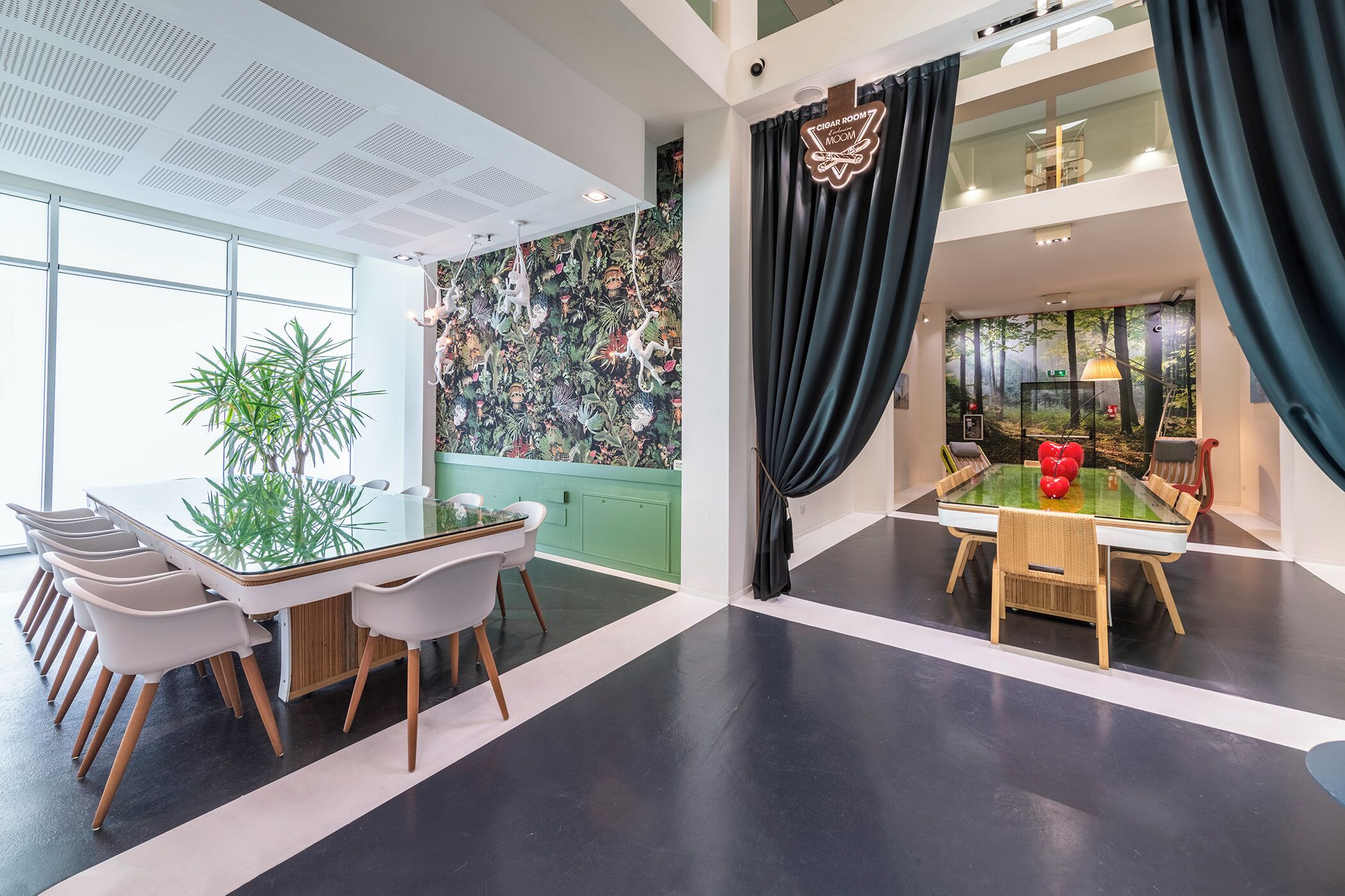 Una habitación de hotel moderna con un ventanal grande, una pared de acento verde, un techo con patrón de cuadrícula y vistas a un bosque desde la ventana.