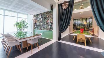 Una habitación de hotel moderna con un ventanal grande, una pared de acento verde, un techo con patrón de cuadrícula y vistas a un bosque desde la ventana.