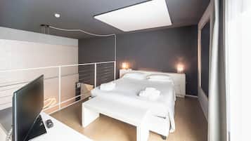 Una habitación de hotel moderna con una cama, mesitas de noche, un escritorio con una computadora y un ventanal grande.