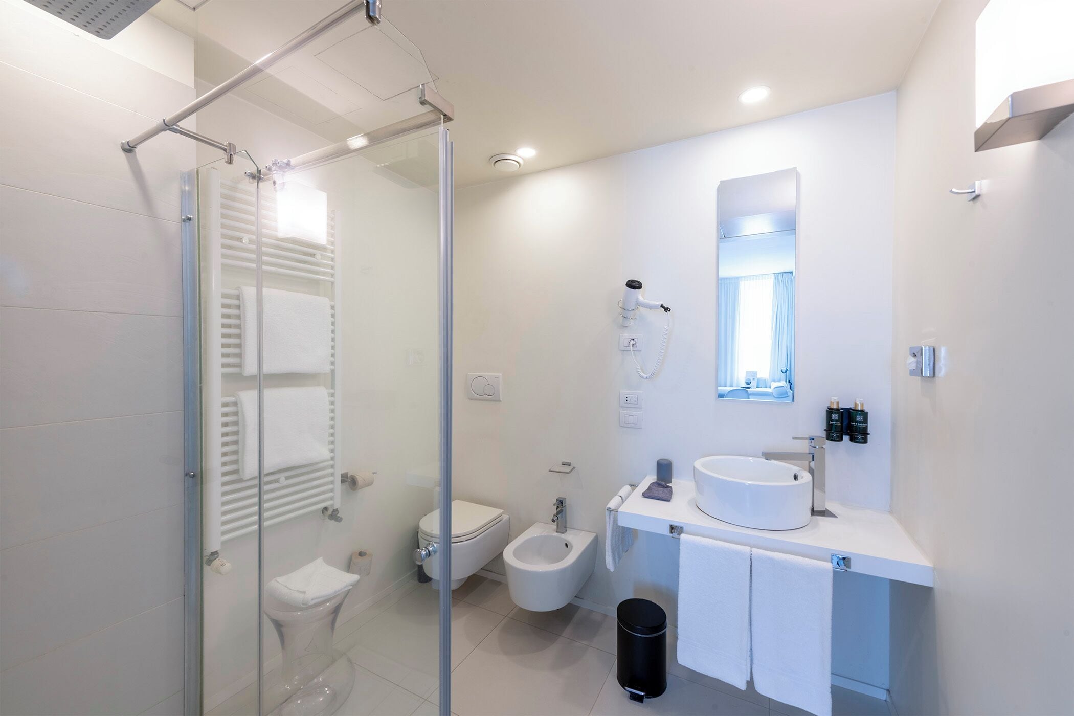 A modern bathroom with a glass shower enclosure, a toilet, bidet, and a sink with a mirror above.