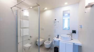 A modern bathroom with a glass shower enclosure, a toilet, bidet, and a sink with a mirror above.
