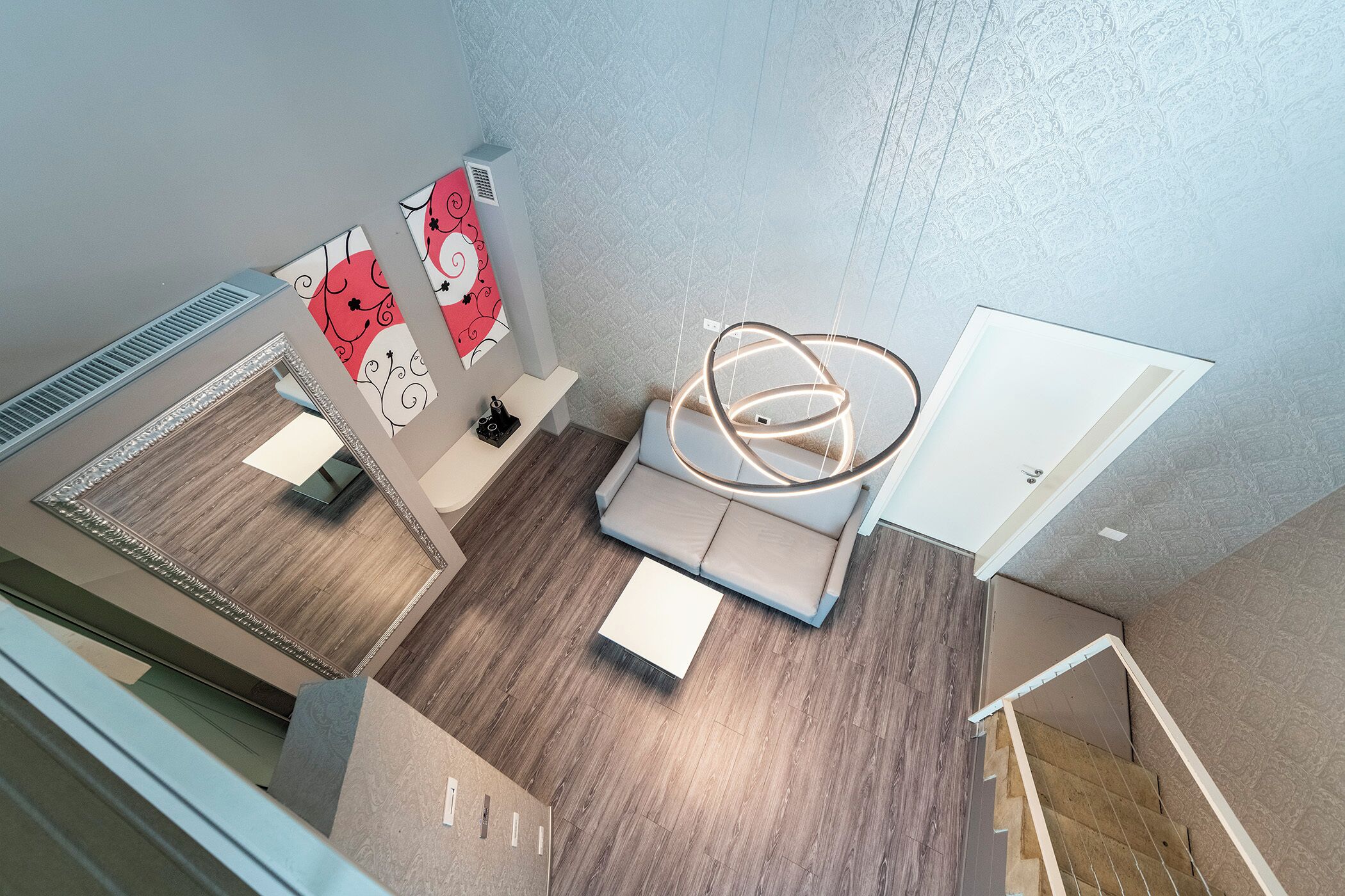 A modern hotel room with a wooden floor, a sofa, a coffee table, and a unique circular light fixture.