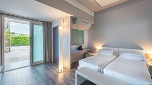 Una habitación de hotel moderna con dos camas, un ventanal grande, una puerta corredera, una mesita de noche y un estante empotrado.