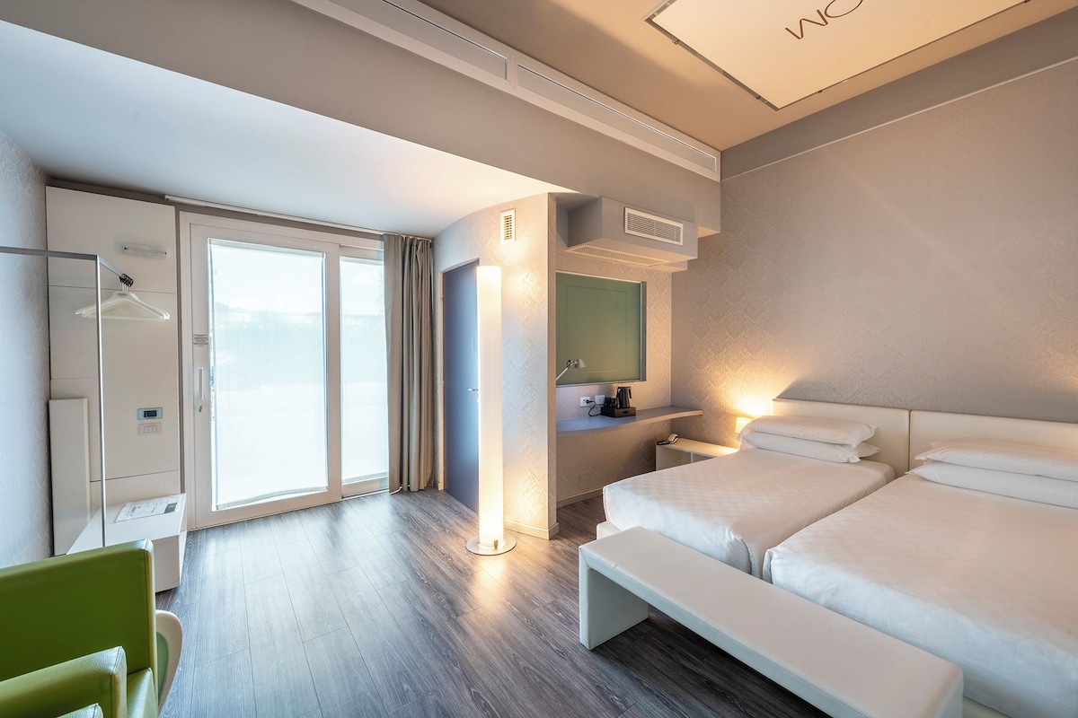 Una habitación de hotel moderna con una cama grande, una mesita de noche, un espejo y una zona de estar.