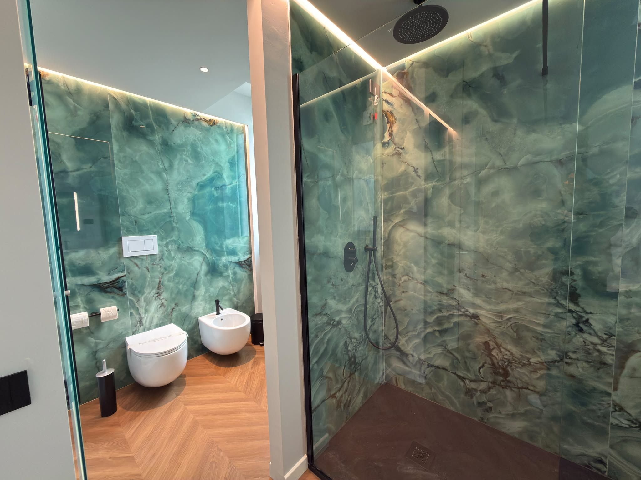 A modern bathroom with a glass shower enclosure, two toilets, and a marble backsplash.