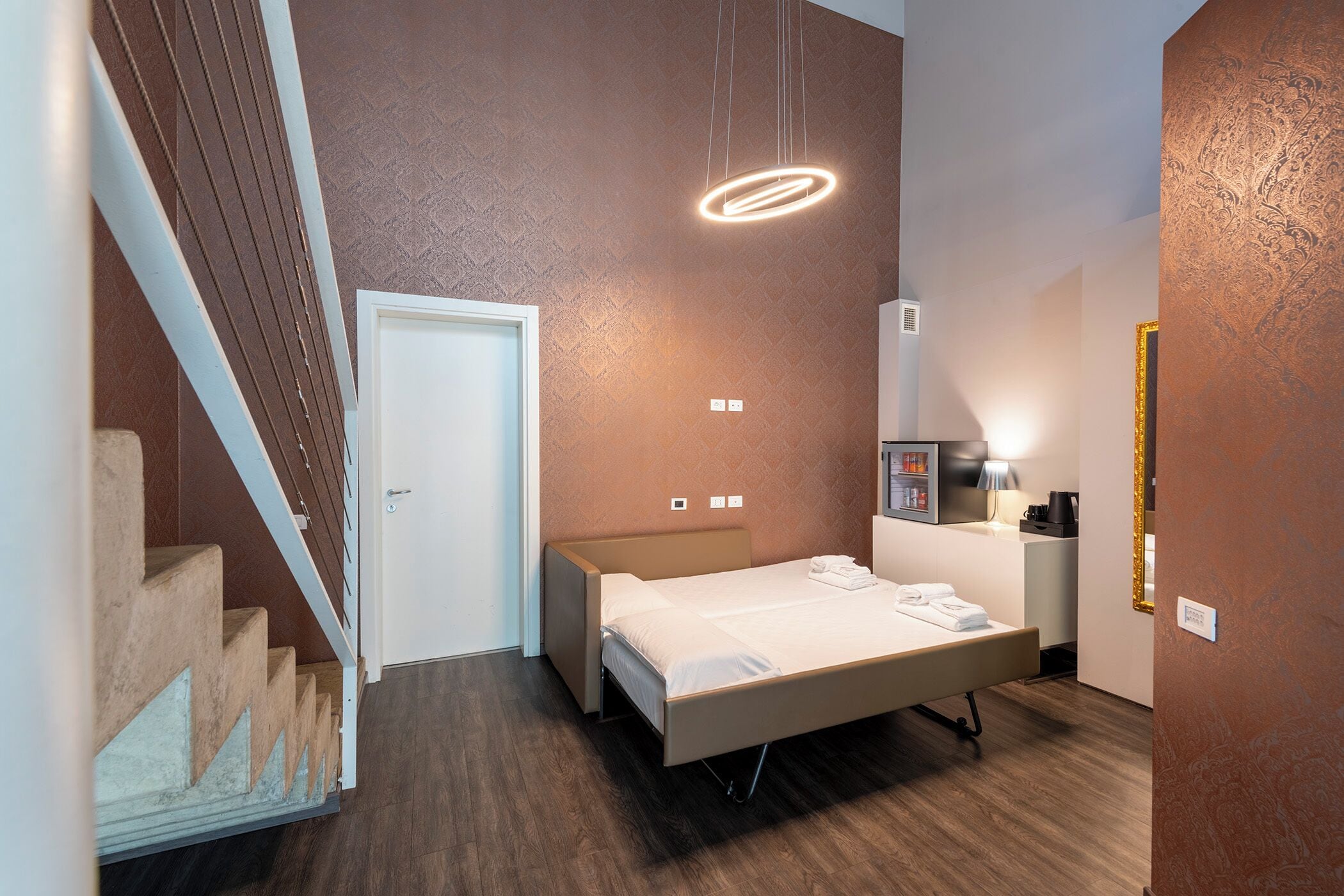 A modern bedroom with a bed, bedside table, lamp, and a staircase.
