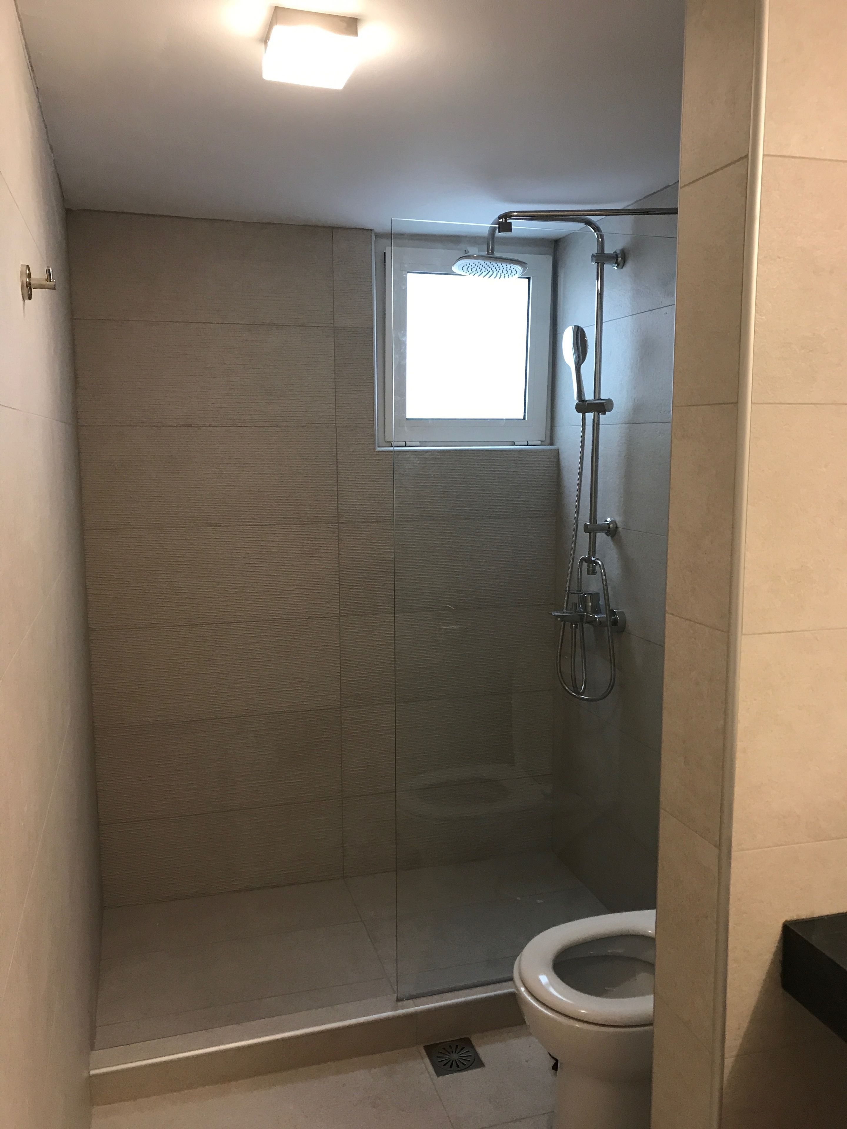 Een kleine, afgesloten douchecel met een glazen deur, een toilet en een raam boven de douche.