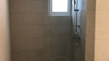 Een kleine, afgesloten douchecel met een glazen deur, een toilet en een raam boven de douche.