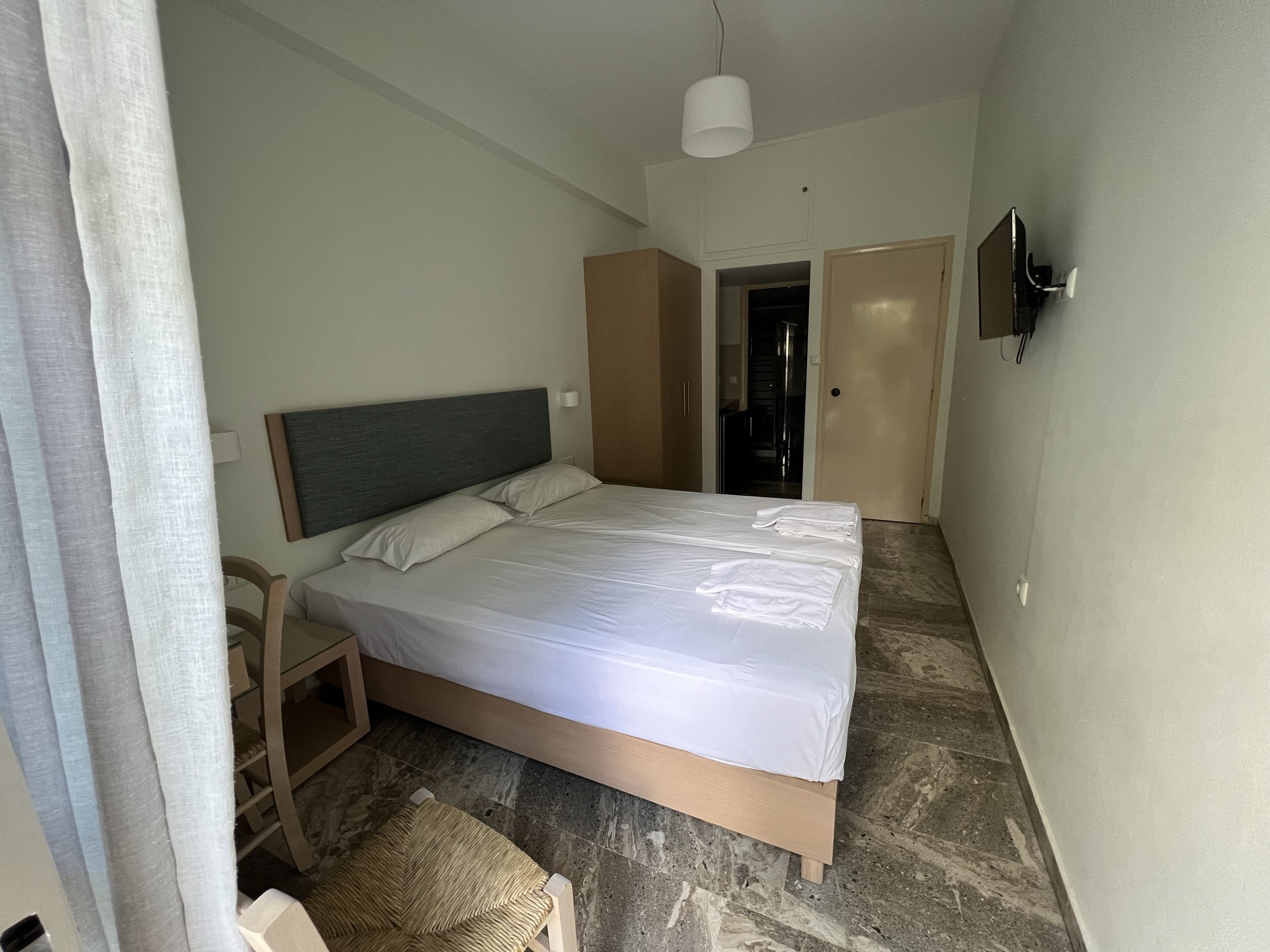 A hotel room with a bed, a chair, a desk, and a wardrobe.