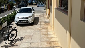 A residential street with a white car parked on the side, a bicycle, and a building with a beige facade.