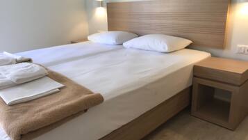 Ein ordentlich bezogenes Bett mit weißen Laken und einer braunen Tagesdecke, ein Holz-Kopfschild und ein kleiner Nachttisch mit Schublade.