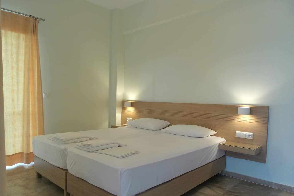 Een net opgemaakt bed met witte lakens en kussens, een houten hoofdbord en bedlampjes.
