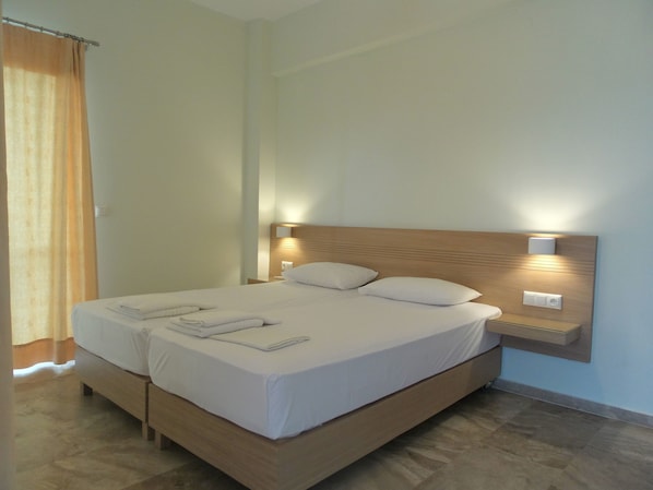 Een net opgemaakt bed met witte lakens en kussens, een houten hoofdbord en bedlampjes.