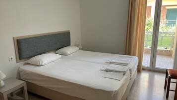 Una cama doble con ropa blanca, una mesita de noche con lámpara y vistas a un balcón con valla verde.