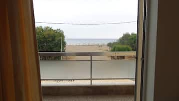 A balcony with a view of a beach, a railing, and a door.