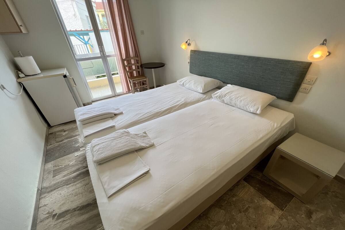 Een hotelkamer met twee bedden, een tafeltje, een stoel en een raam met gordijnen.