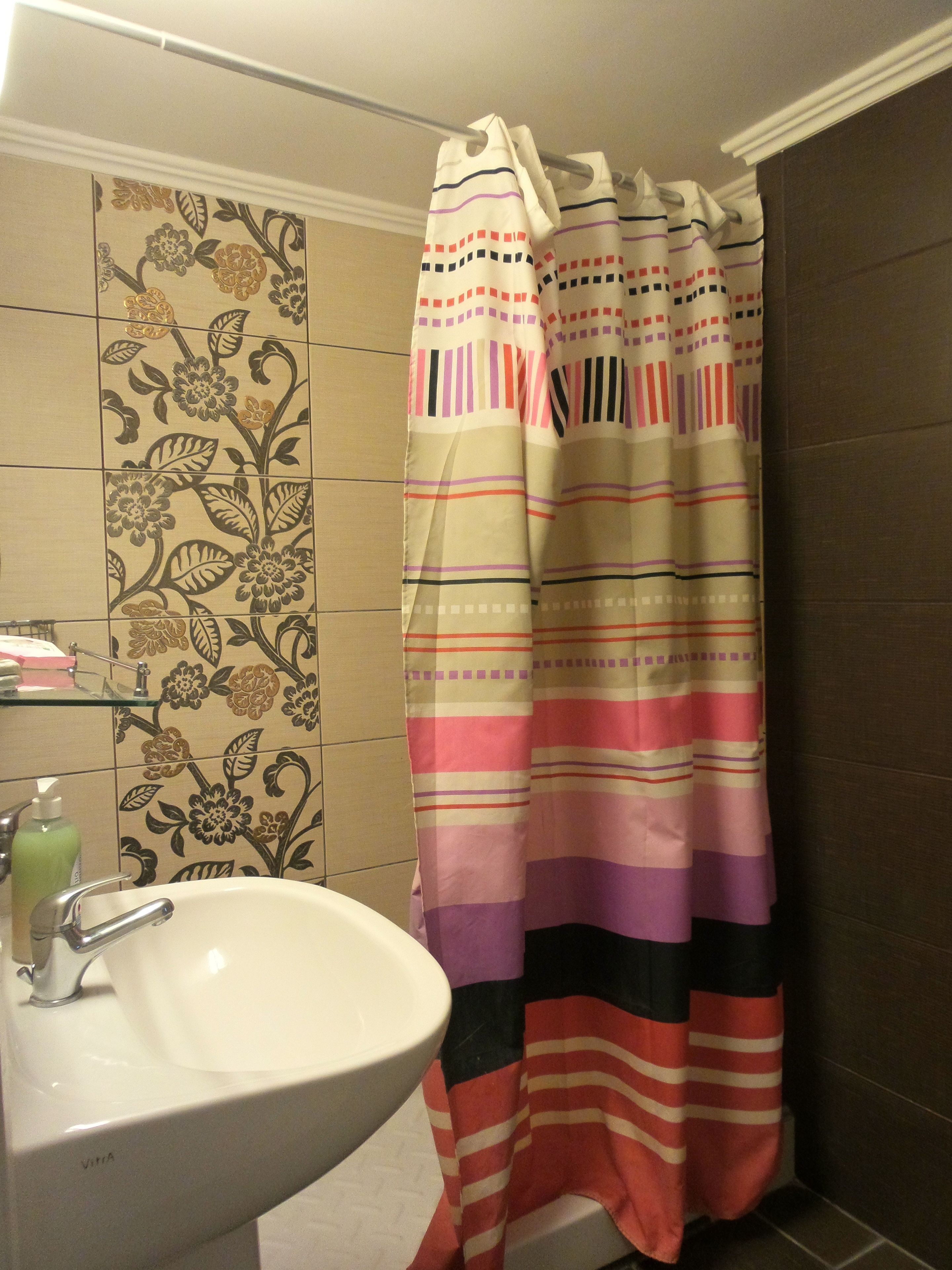A bathroom with a sink, a shower curtain with a striped pattern, and floral tiles on the wall.