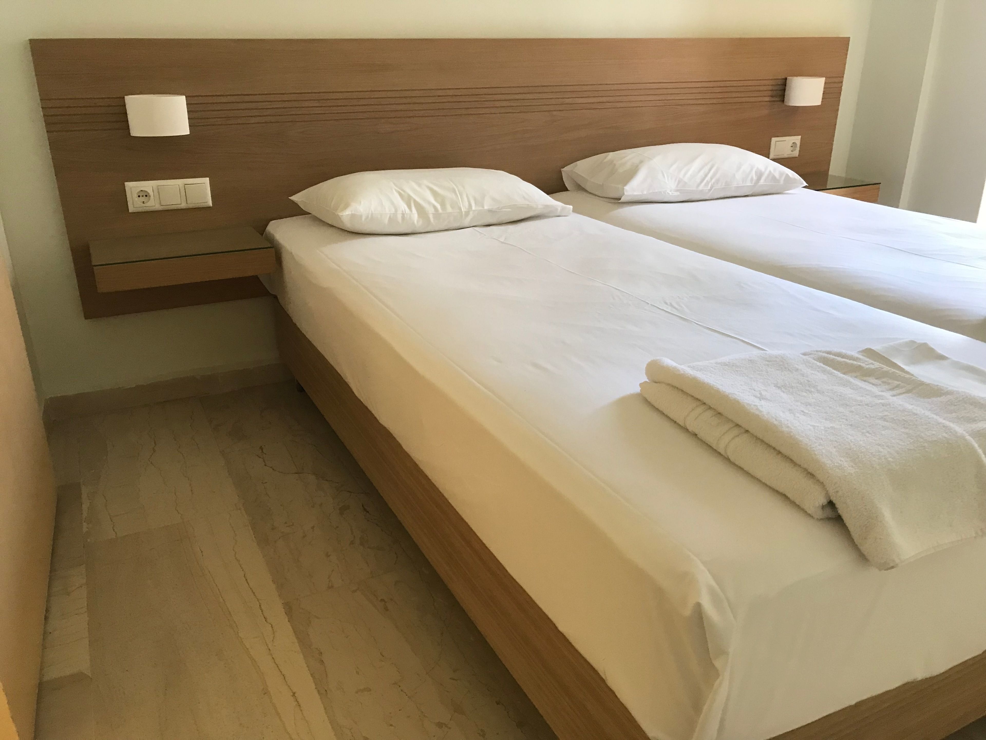 A double bed with a wooden headboard, two bedside tables with lamps, and a folded towel on the bed.