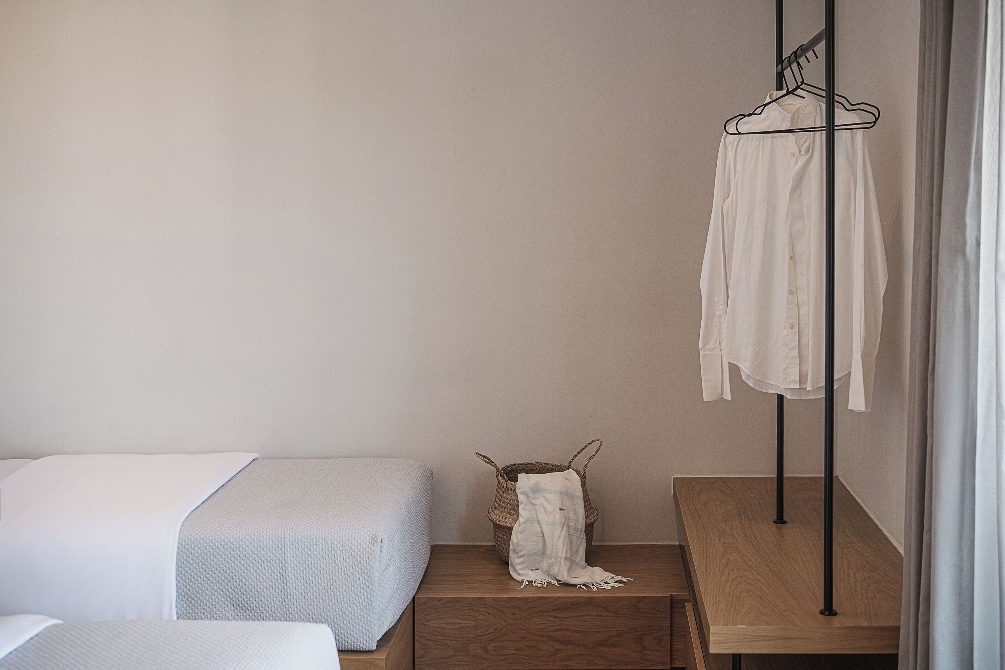 A bedroom with a bed, a wooden nightstand, a woven basket with a blanket, and a clothing rack against the wall.