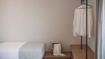 A bedroom with a bed, a wooden nightstand, a woven basket with a blanket, and a clothing rack against the wall.