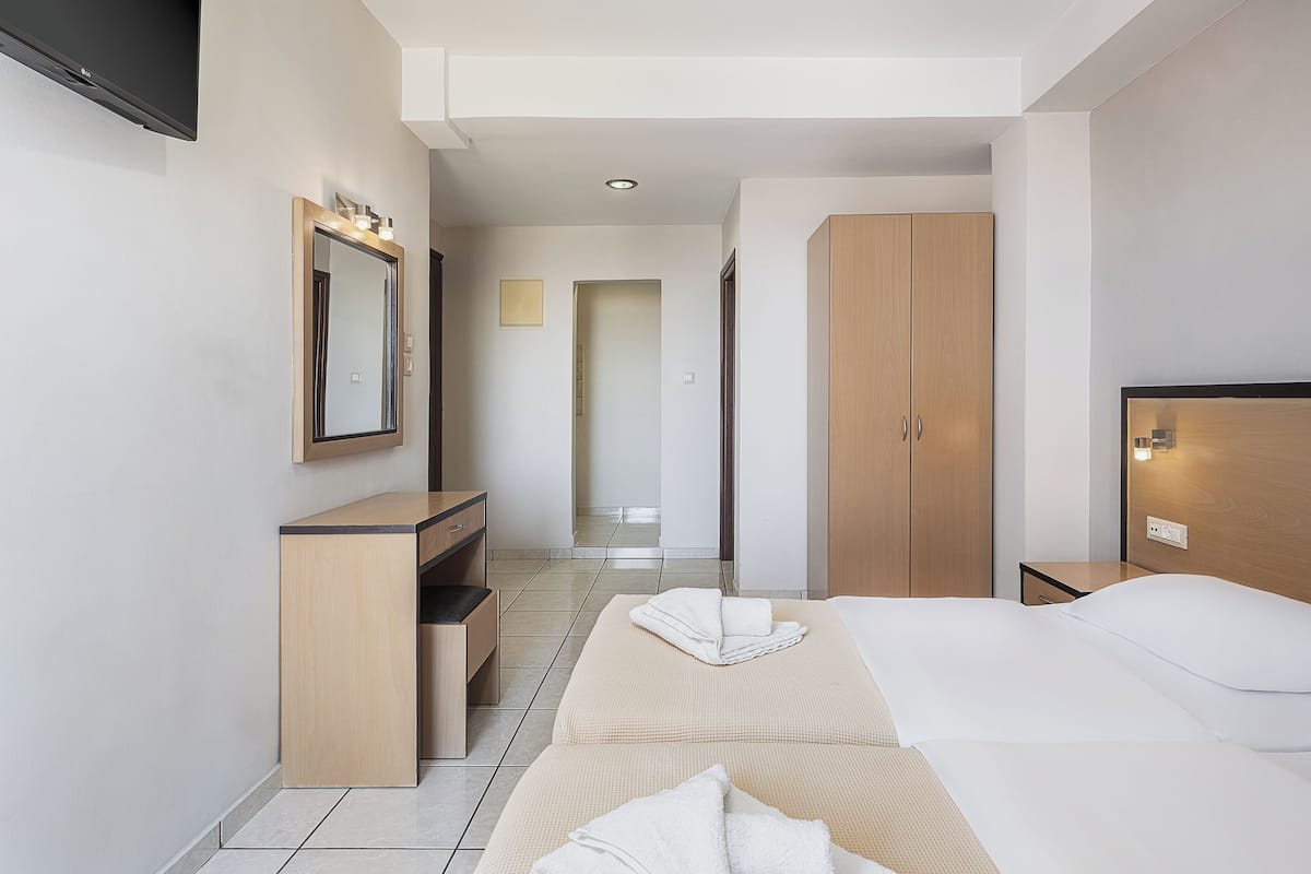 A modern hotel room with a bed, a wooden wardrobe, a vanity with a mirror, and a television mounted on the wall.