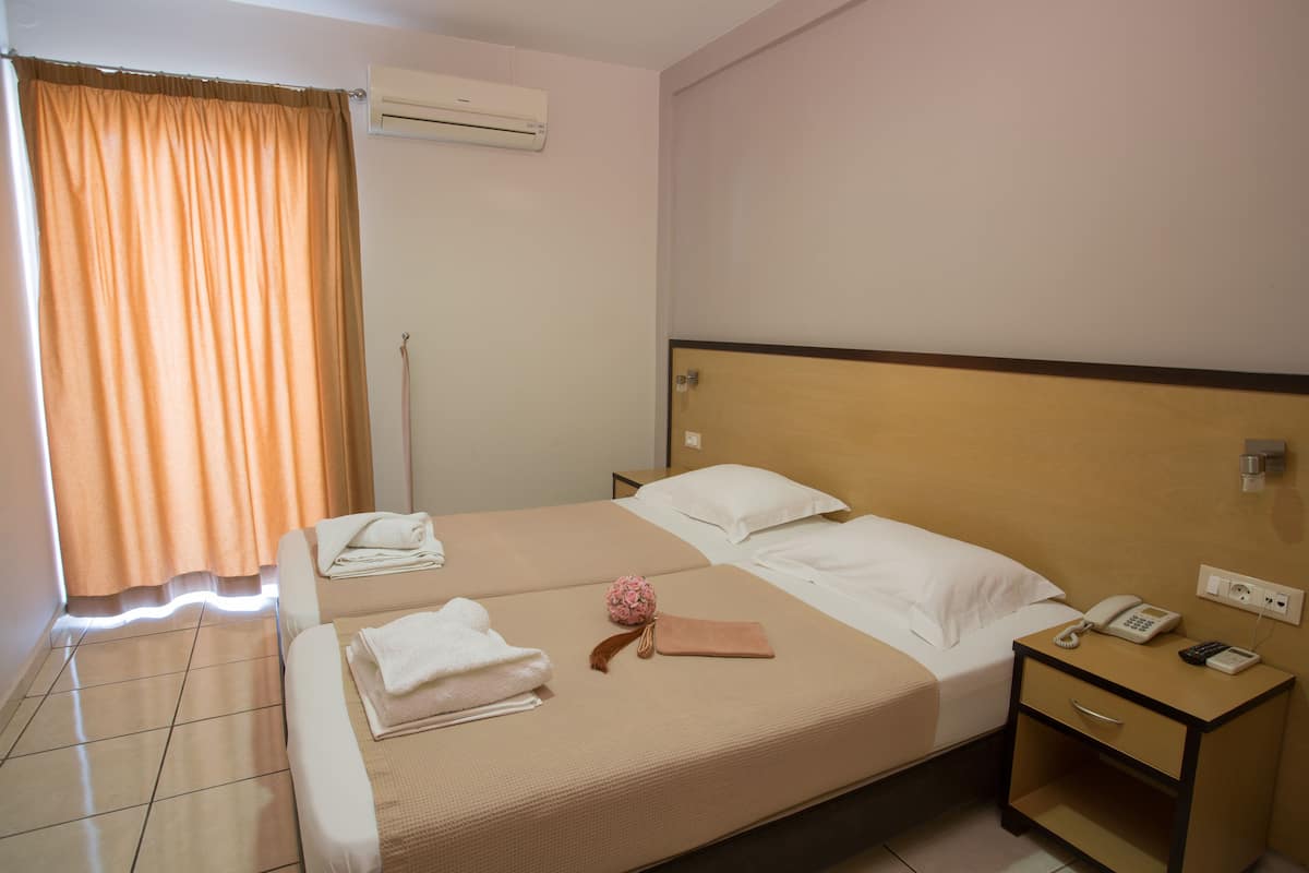 A hotel room with two beds, a bedside table with a phone, and a wall-mounted air conditioner.
