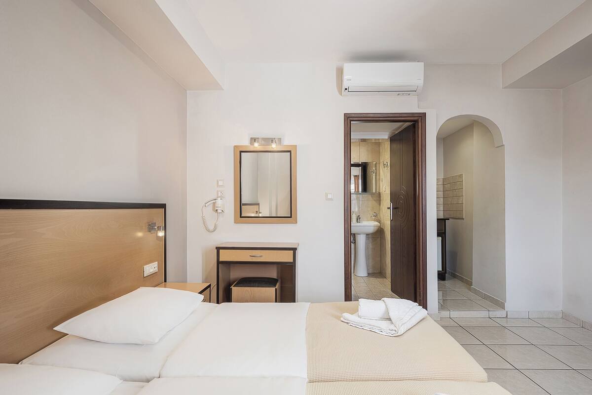 A hotel room with a bed, bedside table, mirror, and an air conditioning unit.