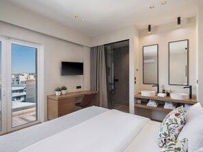 A hotel room with a bed, a desk with a chair, a TV, a shower area, and a bathroom with a sink and mirror. - Theofilos City Hotel (Chania)