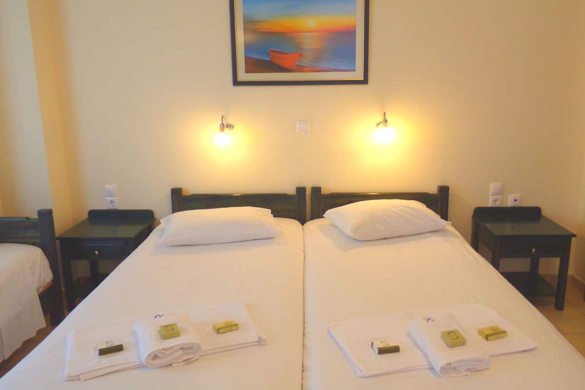 Una habitación de hotel con dos camas, un cuadro en la pared y dos lámparas de noche.