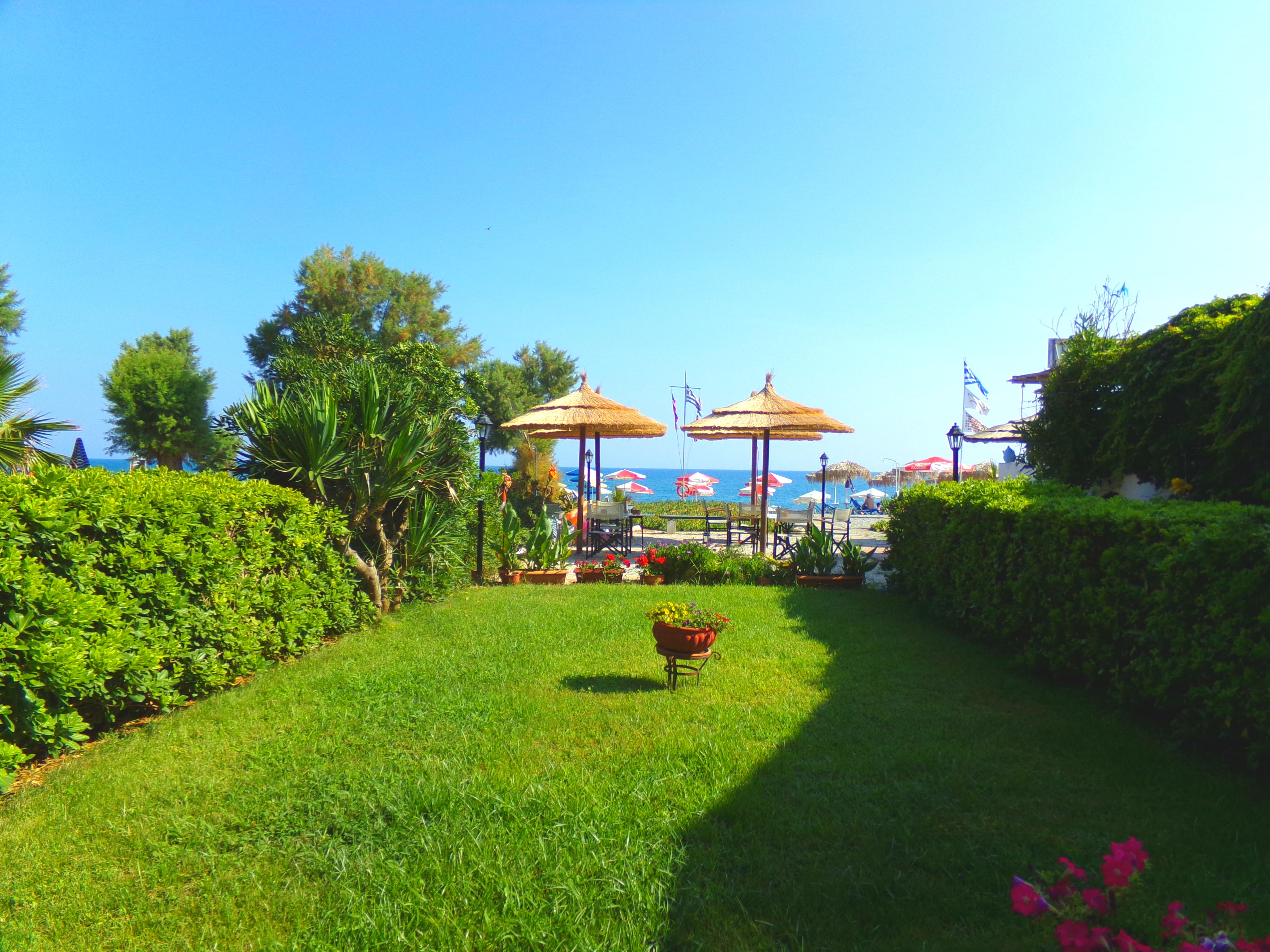 Ein gepflegter Garten mit Rasen, zwei Reetsonnenhüten und Blick aufs Meer.