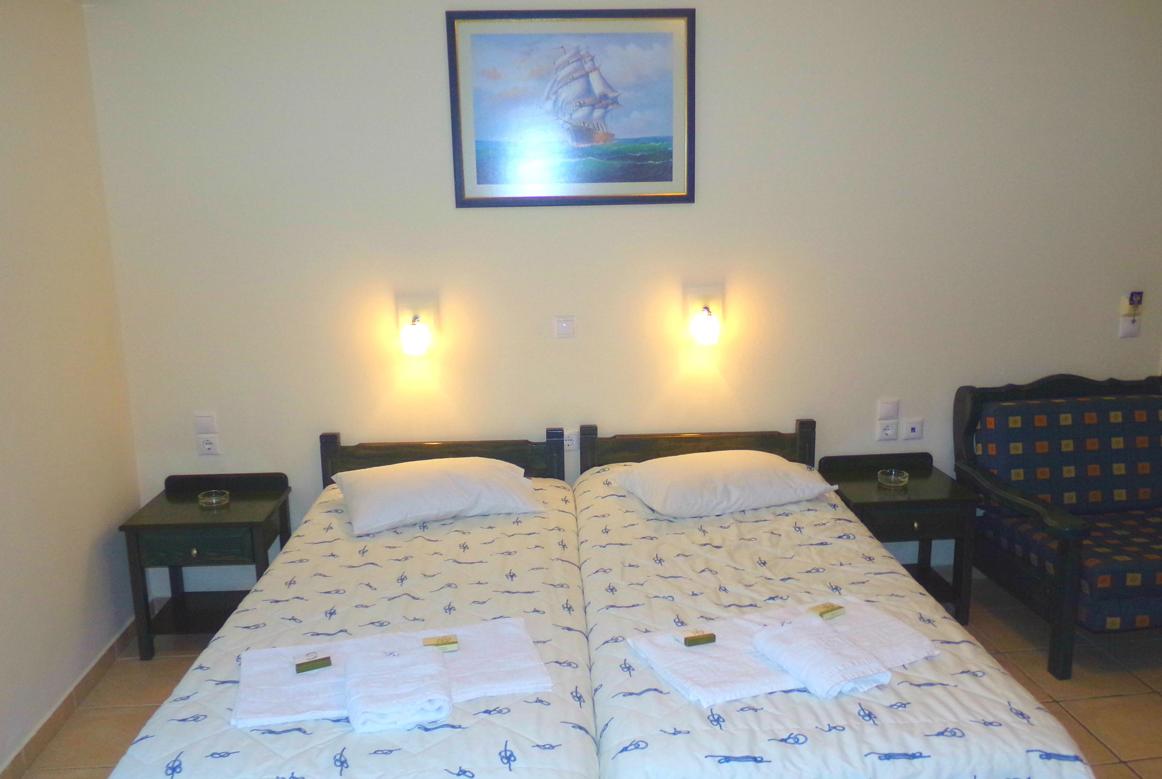 Una cama doble con colcha de temática náutica, dos mesitas de noche con lámparas, un cuadro enmarcado sobre la cama y un sillón estampado a la derecha.