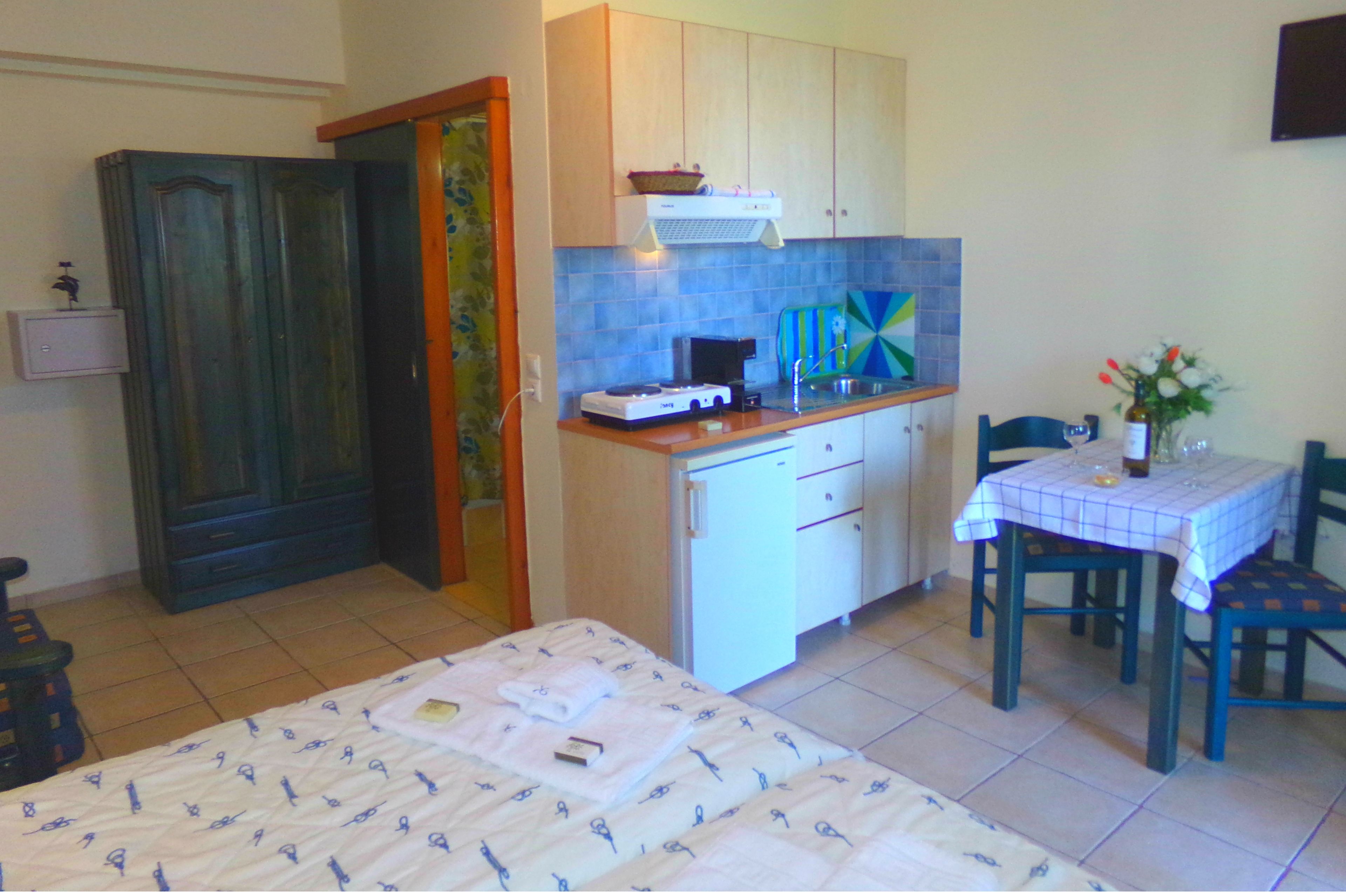 Cocina compacta con comedor, una cama con colcha estampada y una mesita con un jarrón de flores.