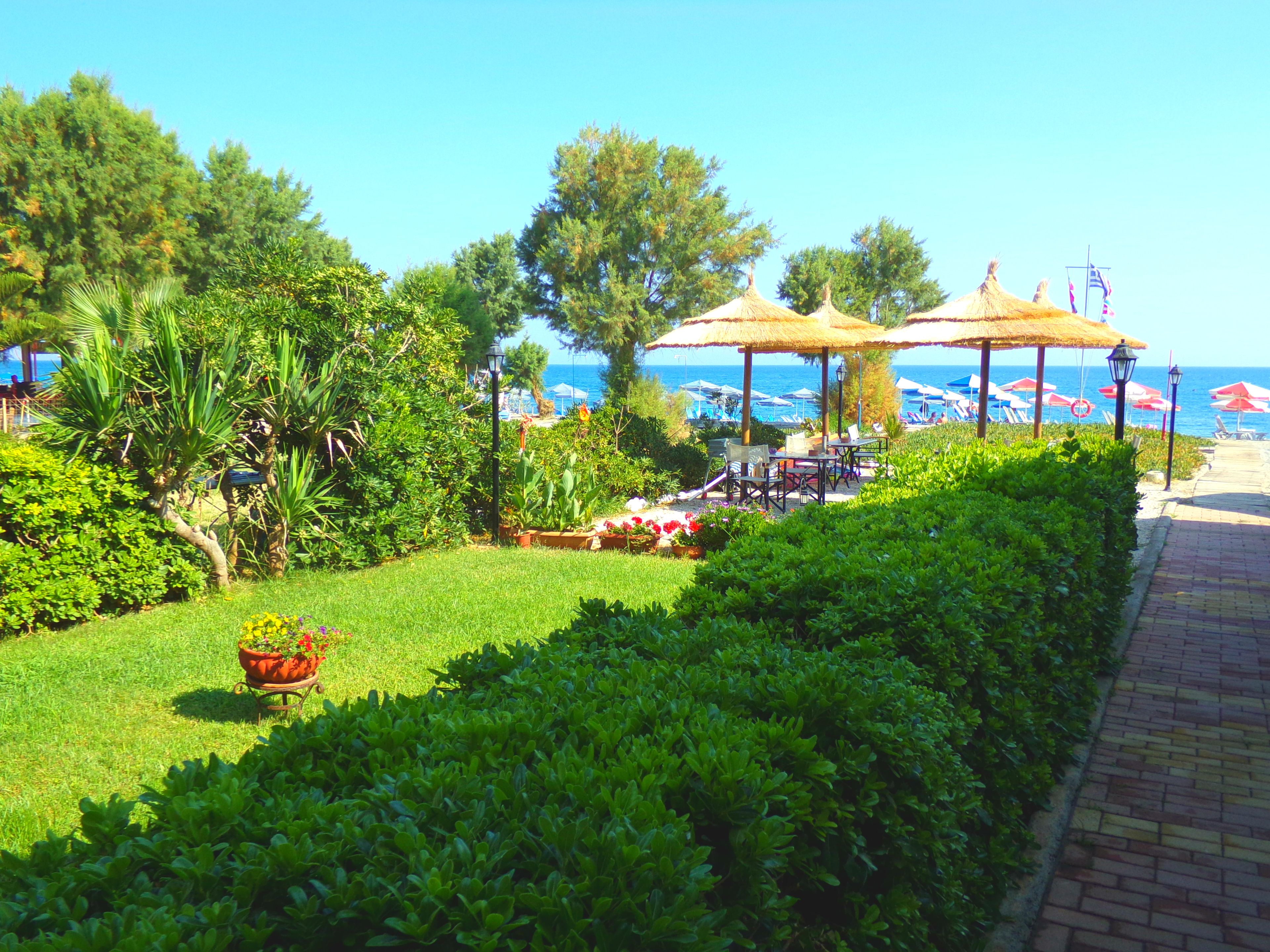 A garden with a pathway, a thatched-roof gazebo, and a view of the sea.