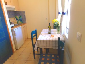 Een compacte keuken met een eettafel, stoelen, een koelkast en een raam met gordijnen.