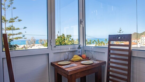 Un balcon avec une table en bois, dressée pour deux personnes, une chaise et une vue sur la mer et les bâtiments.