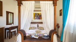 Un lit à baldaquin avec des rideaux blancs, un bureau en bois avec un miroir et un tableau accroché au mur.