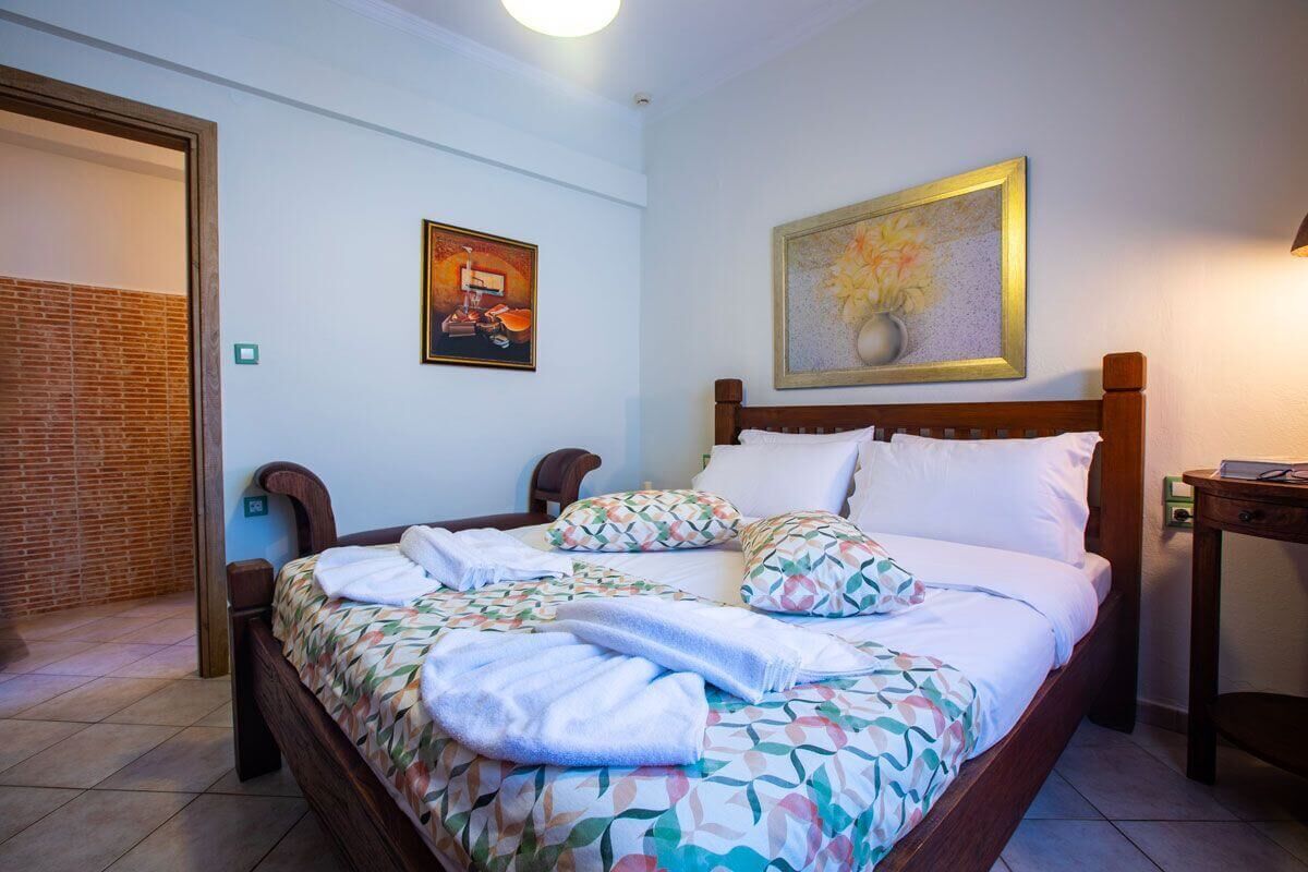 A neatly made bed with a floral bedspread and pillows, a wooden headboard, and two framed artworks on the wall.