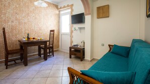 Un salon avec un mur en briques, une table à manger en bois avec des chaises, un canapé de couleur turquoise et un téléviseur fixé au mur.