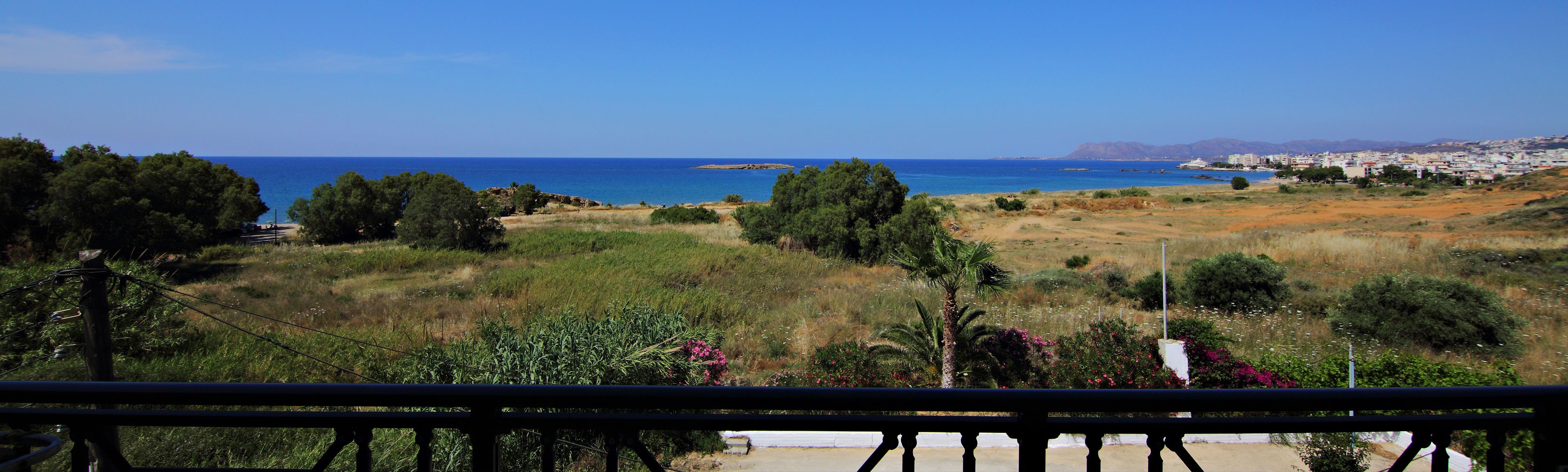 Un paisaje costero con vista al mar, una zona verde con árboles y un pueblo lejano.