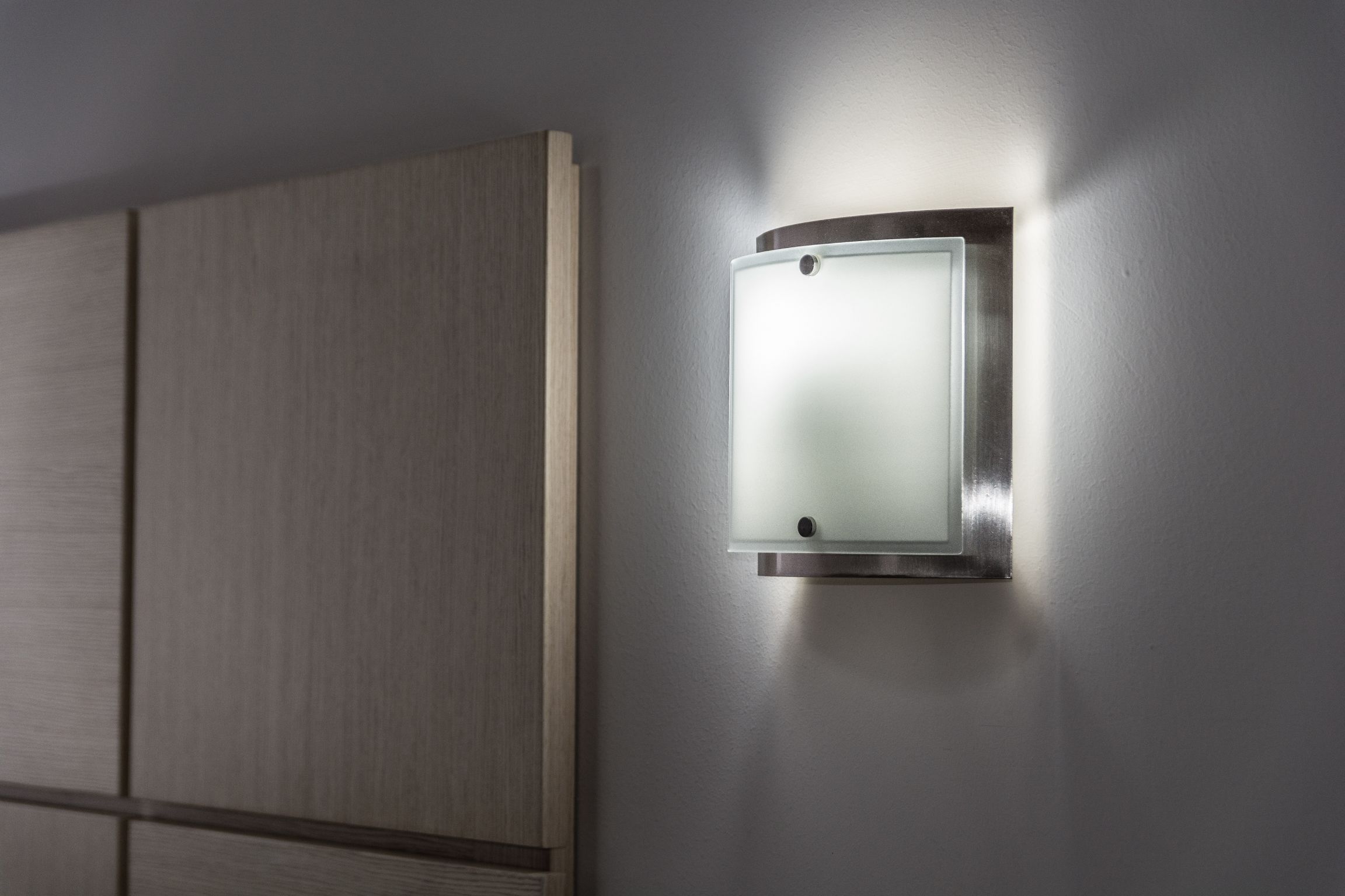 Un luminaire mural doté d’un panneau en verre dépoli, fixé sur un mur orné de panneaux en bois.